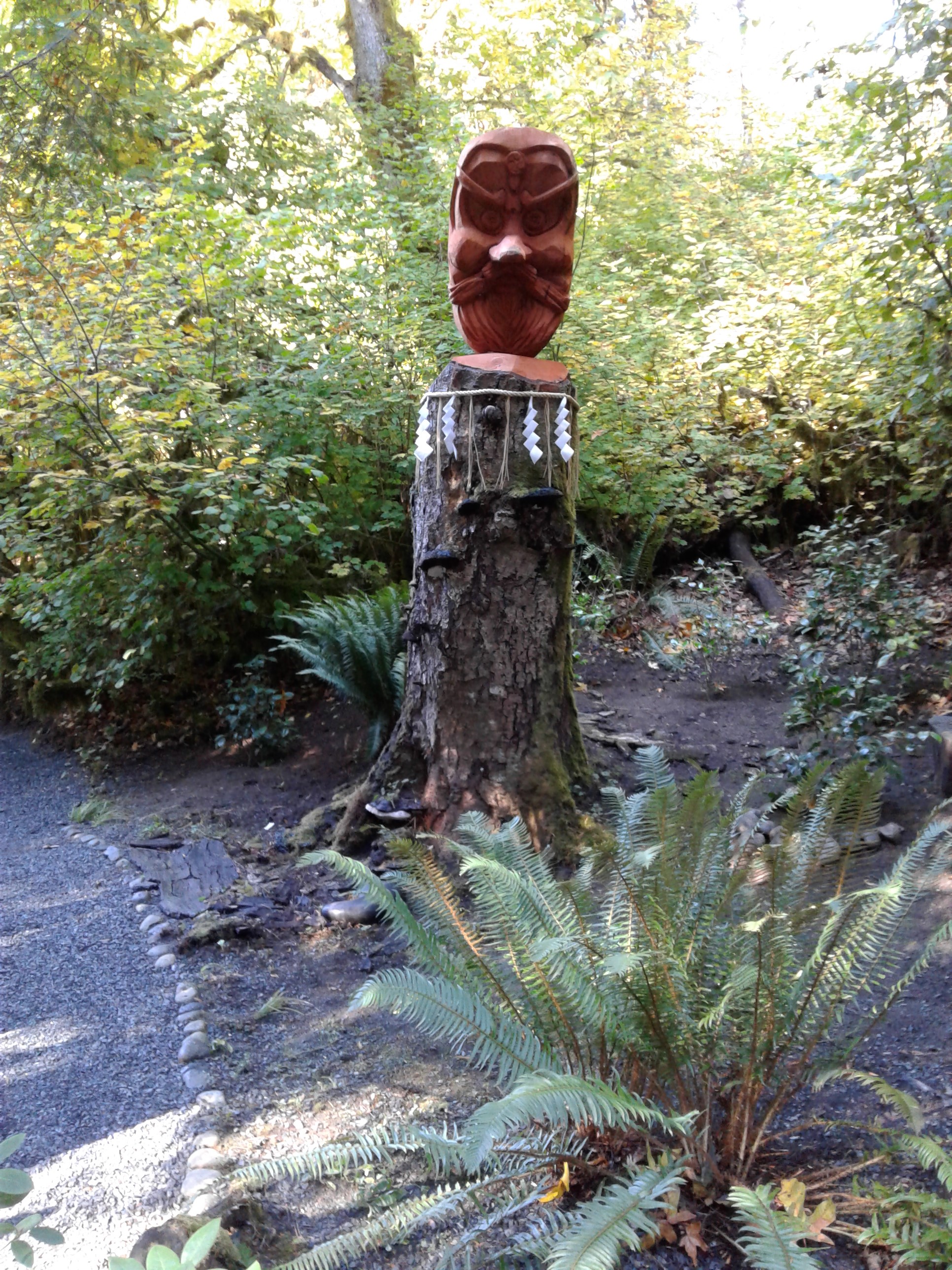 carved mask on top of tree stump, surrounded with rice ropes and shade (zig zag paper strips)